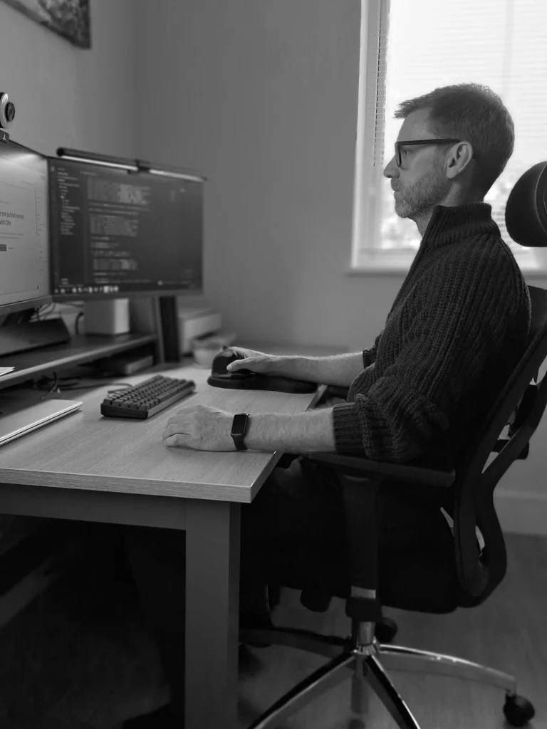 Matthew Day sitting at a dual monitor workstation desk setup, focused on a screen.