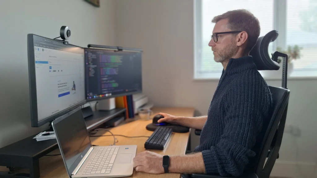Matthew Day sitting at a multi monitor workstation desk setup, focused on a screen.
